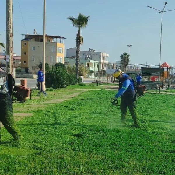 Akdeniz Belediyesi ekipleri bir parkta çim biçme çalışması yapıyor.